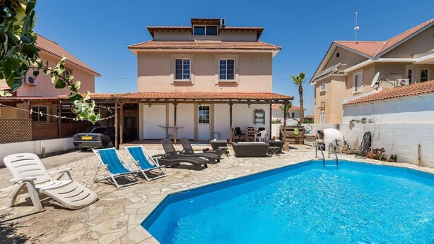 A pool area with lounge chairs, a covered seating area, and a two-story building with a tiled roof. - 4 Bedroom Villa With Private Pool Near Beach (Oroklini)