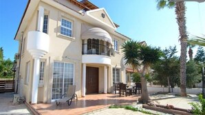 A two-story house with a balcony, a patio with outdoor furniture, and a garden with palm trees. - 4 Bedroom Villa With Private Pool Near Beach (Oroklini)