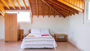 A bedroom with a sloped ceiling, wooden beams, a bed with a striped blanket, a wardrobe, and a window. - 4 Bedroom Villa With Private Pool Near Beach (Oroklini)