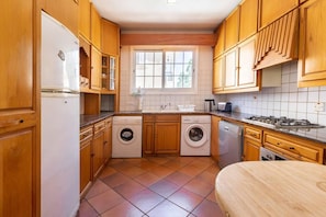 A compact kitchen with wooden cabinets, a washing machine, a dishwasher, a stove, and a window providing natural light.