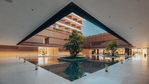 Un vaste atrium intérieur agrémenté d’un bassin d’eau décoratif, doté d’une architecture moderne et offrant une vue sur un immeuble avec des balcons.