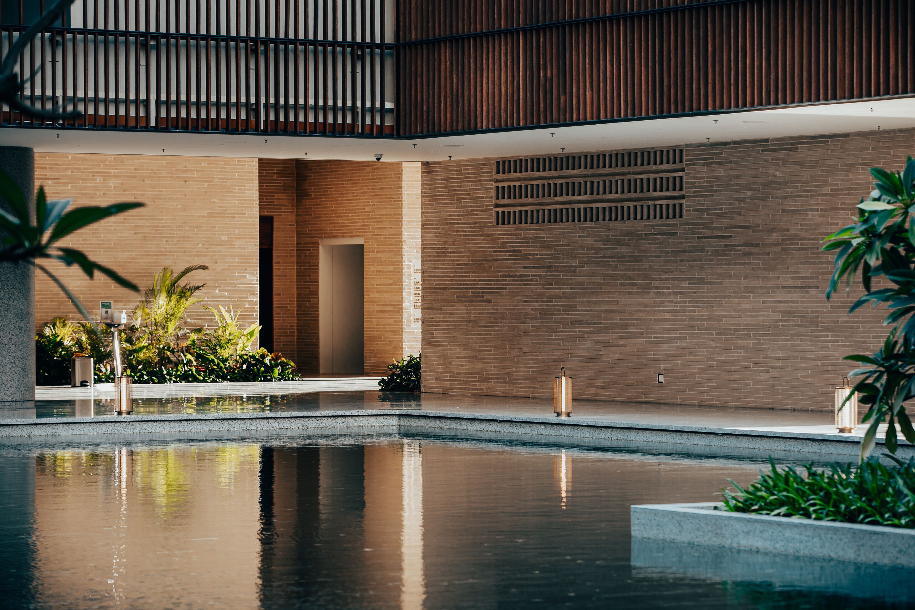 A modern indoor pool area with a brick wall, a wooden ceiling, and potted plants.