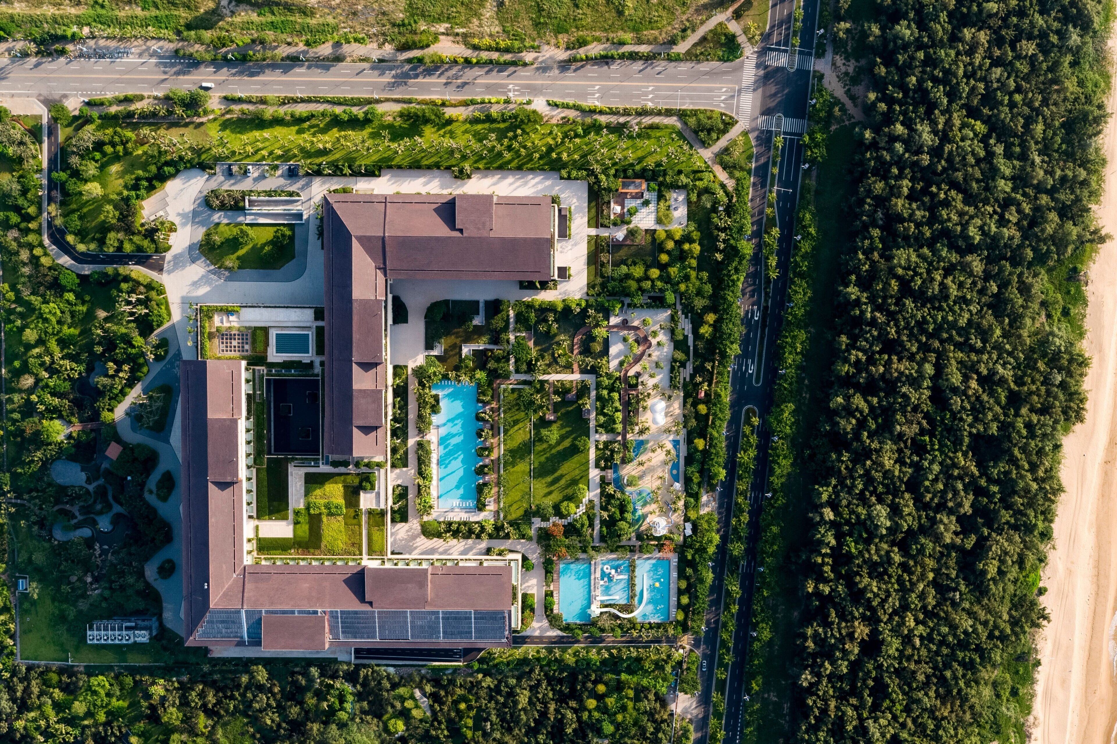 An aerial view of a resort with multiple swimming pools, a large building, and surrounding greenery.