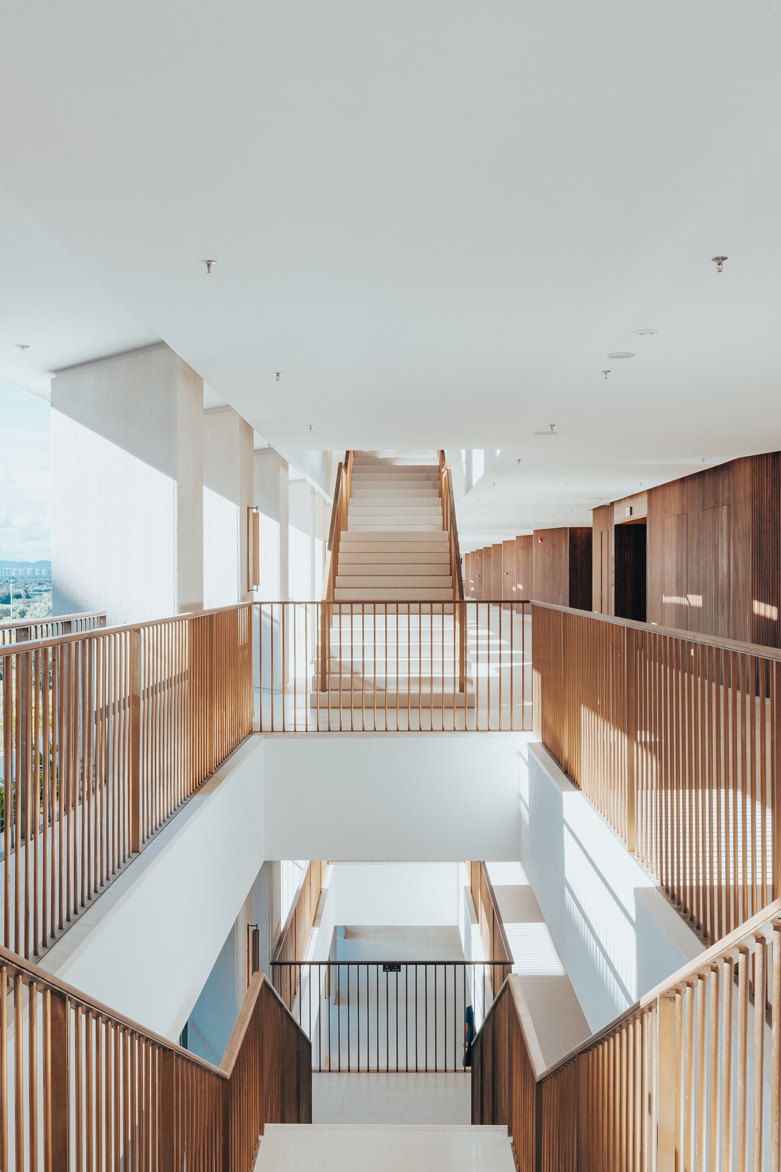 A multi-level interior with a central staircase, wooden railings, and a view of the city.