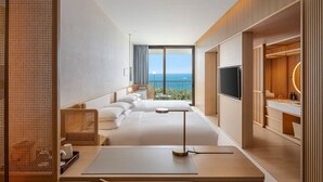 Une chambre d’hôtel moderne dotée d’un grand lit, d’un bureau, d’une télévision et d’un balcon offrant une vue sur la mer.