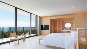 Une chambre d’hôtel moderne dotée d’un grand lit, d’une télévision, d’un balcon avec vue sur la mer et d’une petite table avec des chaises.