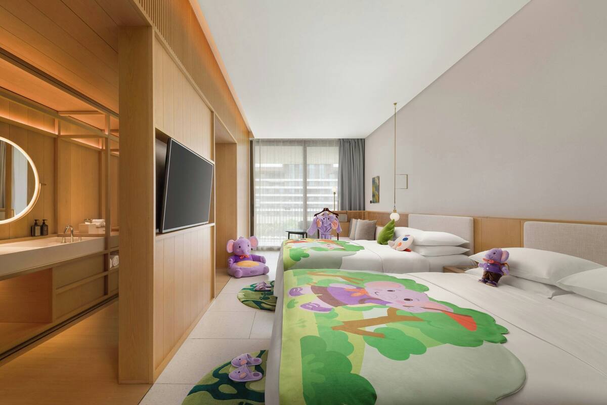 A modern hotel room with a large bed, a TV, a wooden vanity, and a window with curtains.