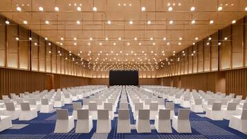A large conference room with rows of white chairs, a blue carpet, and a stage at the front.