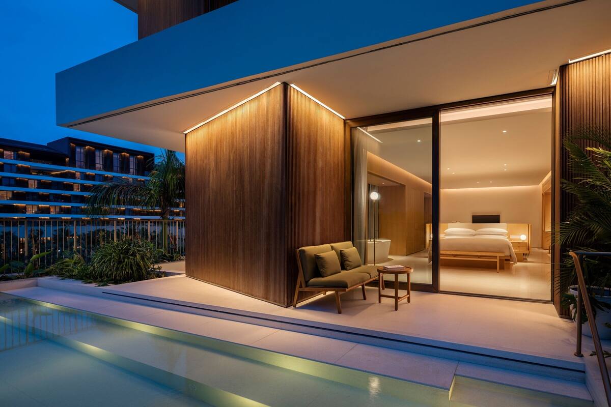 A modern hotel room with a glass door, a sofa, a small table, and a bed.