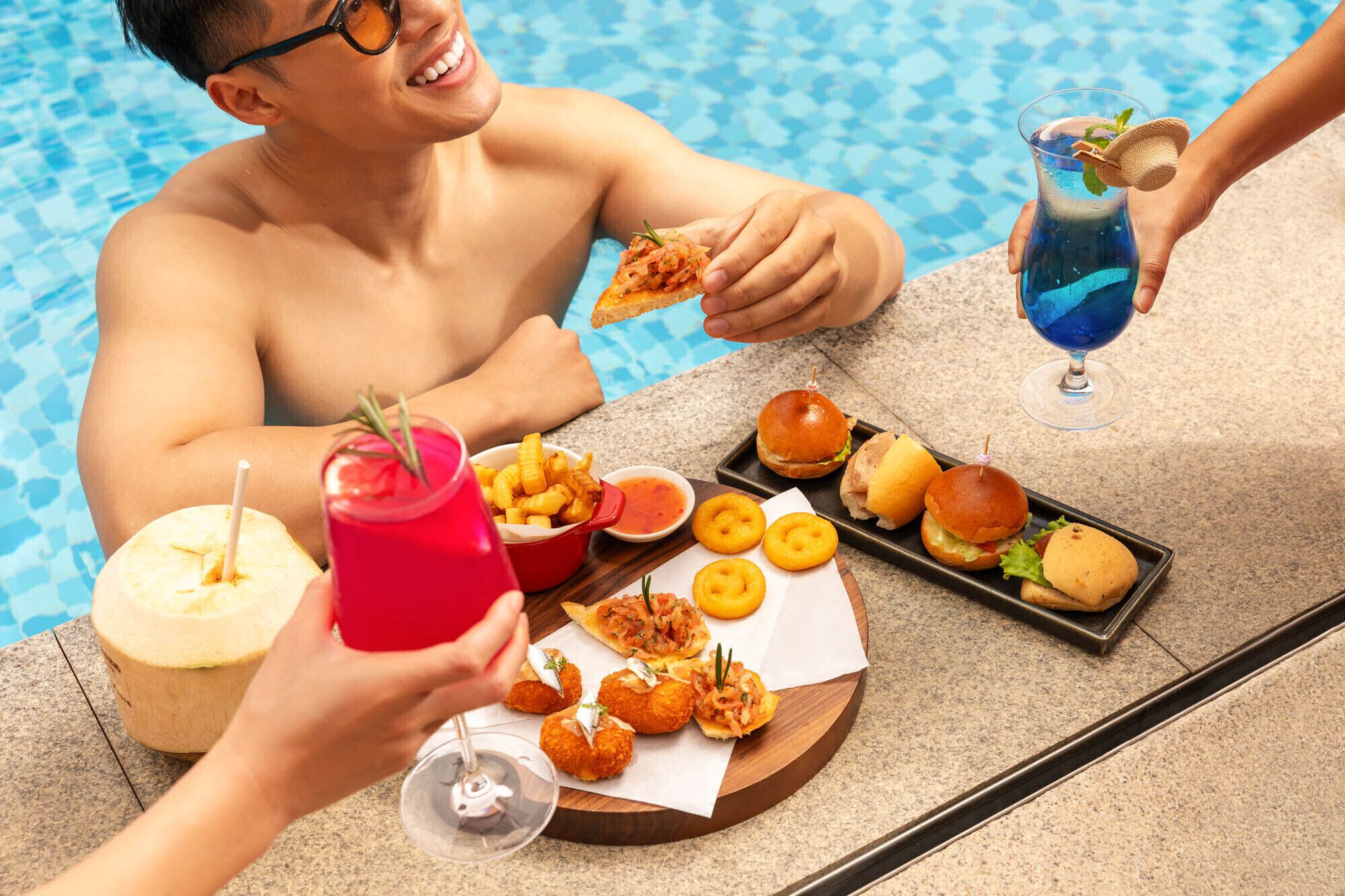 Zona de comedor junto a la piscina con una mesa preparada para dos personas, mostrando una variedad de comida y bebidas.