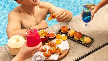 Zona de comedor junto a la piscina con una mesa preparada para dos personas, mostrando una variedad de comida y bebidas.