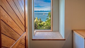 A room with a wooden slatted wall and a small window overlooking a body of water with distant mountains. - Roydons - Kaiteriteri Upstairs Holiday Unit (Kaiteriteri)