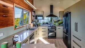 A modern kitchen with a large window, built-in appliances, and a wooden accent wall. - Roydons - Kaiteriteri Upstairs Holiday Unit (Kaiteriteri)