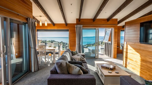 A modern living room with a sofa, coffee table, and a view of the sea. - Roydons - Kaiteriteri Upstairs Holiday Unit (Kaiteriteri)