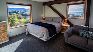 Een slaapkamer met een bed, twee nachtkastjes, een slaapbank en grote ramen met uitzicht op een landschap.
