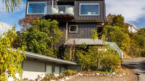 Een modern huis met twee verdiepingen en een balkon, omringd door weelderige begroeiing en een grindpad.