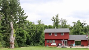Ein rotes Haus mit Terrasse, einem großen Baum und einem Rasen.
