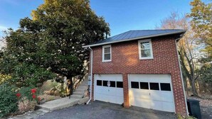 A two-story brick house with a garage, surrounded by trees and a clear sky.