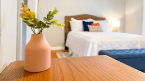 A hotel room with a bed, pillows, a bedside table, and a vase with flowers.