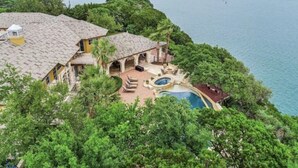 Une grande maison avec une piscine, entourée d’une végétation luxuriante et donnant sur un plan d’eau.