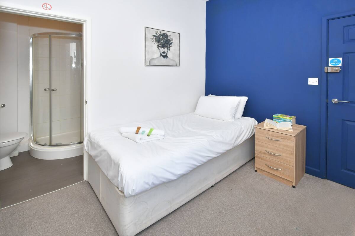 Une chambre à coucher avec un lit, une commode en bois, une porte bleue et un espace douche.