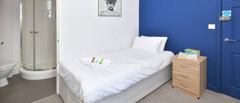 A bedroom with a bed, a wooden dresser, a blue door, and a shower area.