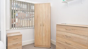 A bedroom with a wooden wardrobe, a bedside cabinet, and a window with blinds. - Townhouse @ 115 Walthall Street Crewe (Crewe)