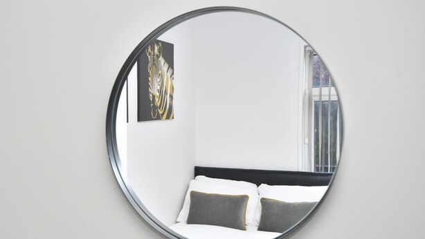 A circular mirror reflecting a bed with white and gray bedding, a black headboard, and a wall-mounted artwork. - Townhouse @ 115 Walthall Street Crewe (Crewe)