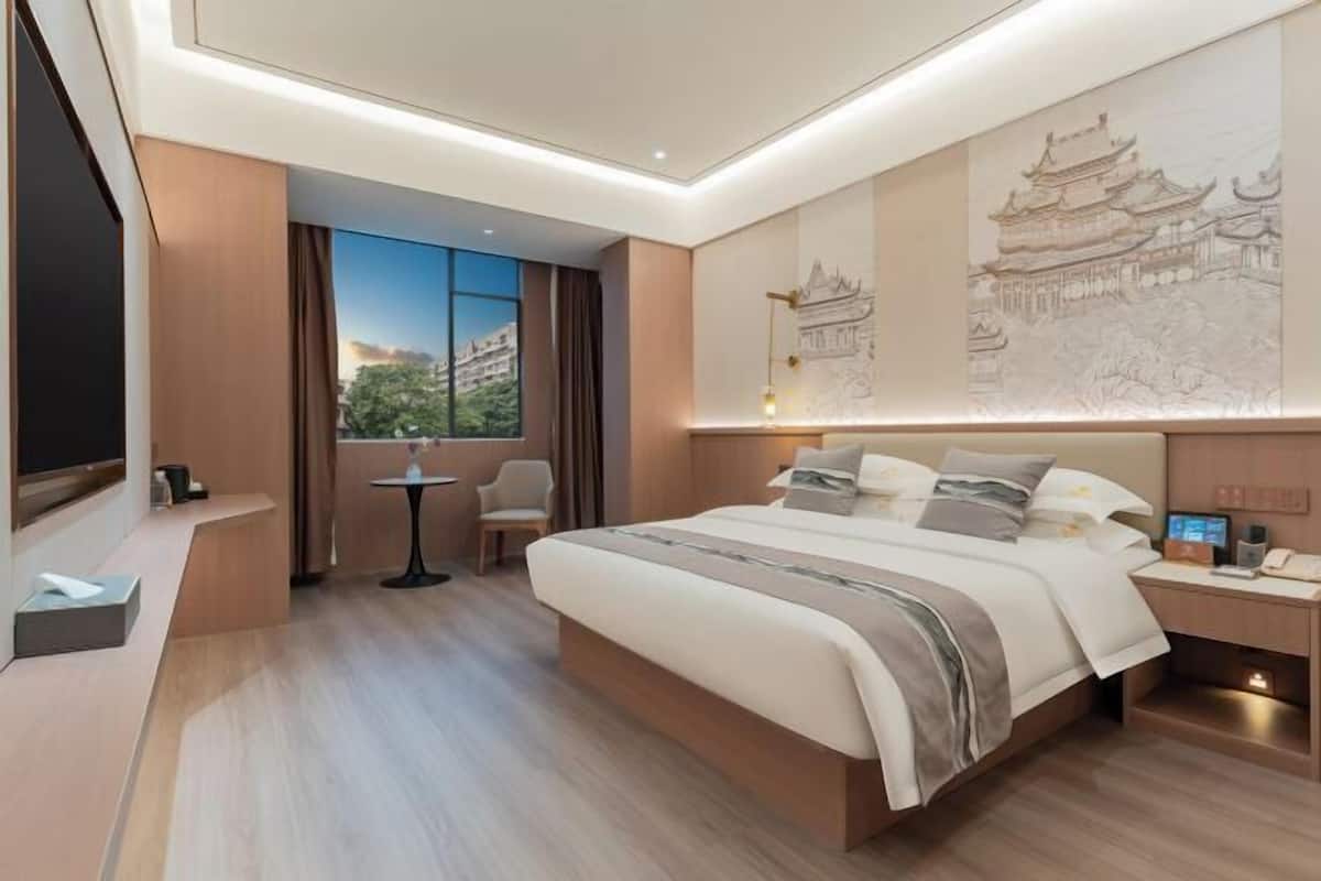 A hotel room with a large bed, a desk, a chair, a small table, and a window with a view.