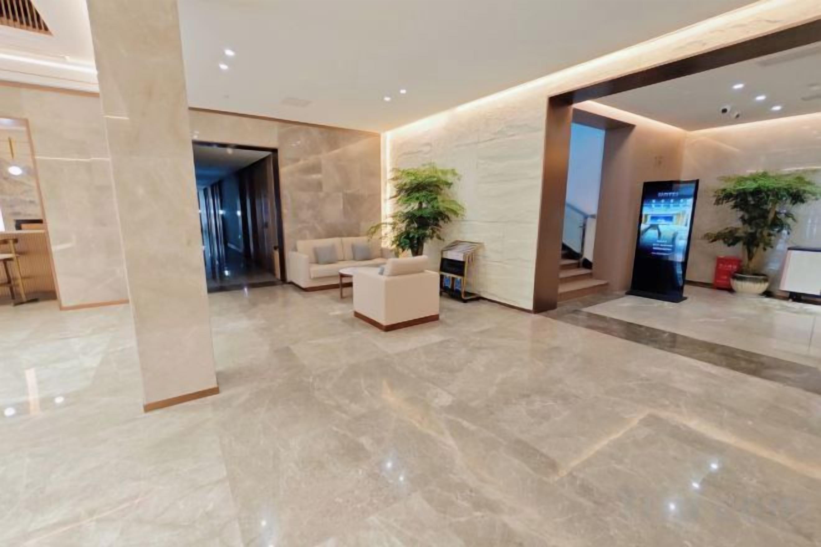 A modern lobby with a marble floor, a reception desk, seating area, and a staircase.