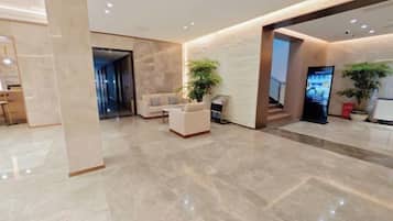 A modern lobby with a marble floor, a reception desk, seating area, and a staircase.