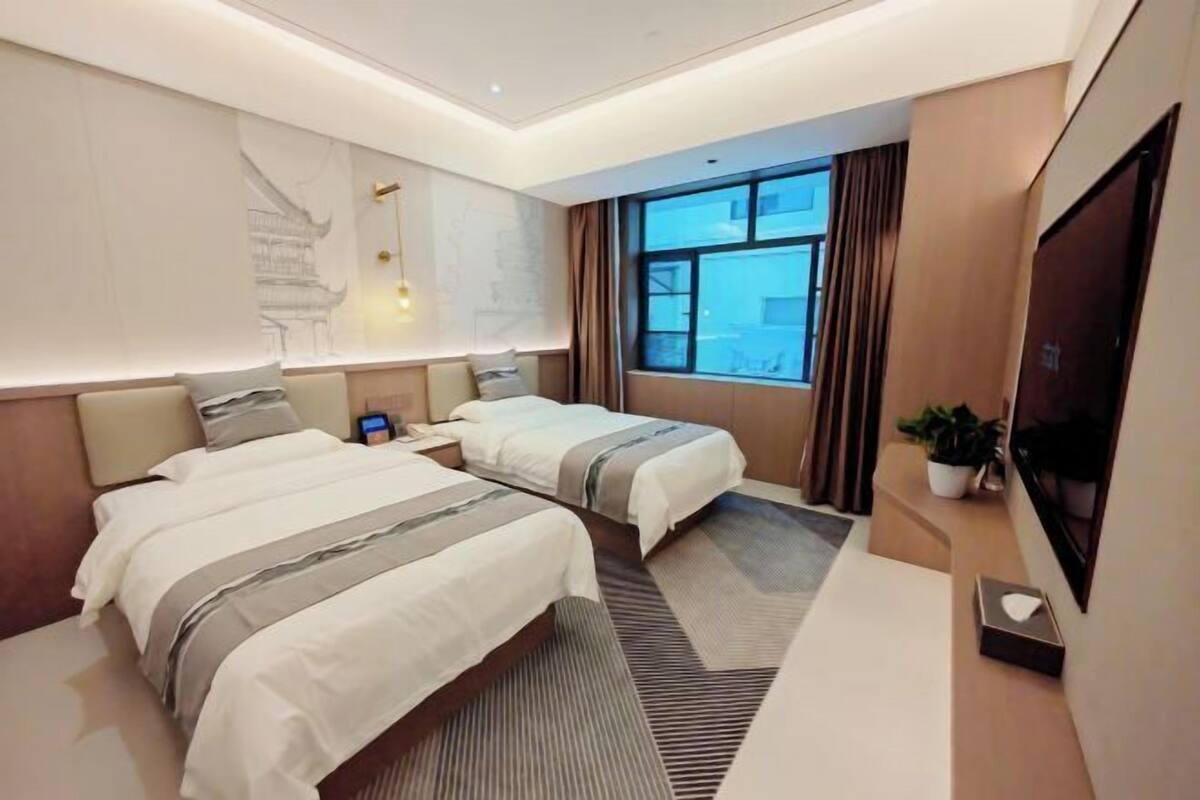 A hotel room with two beds, a large window, a flat-screen TV, and a wall-mounted artwork.