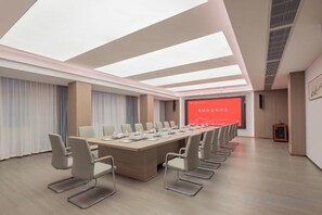 Un salón de conferencias con una larga mesa, sillas, una pantalla de proyector y una pantalla para presentaciones.