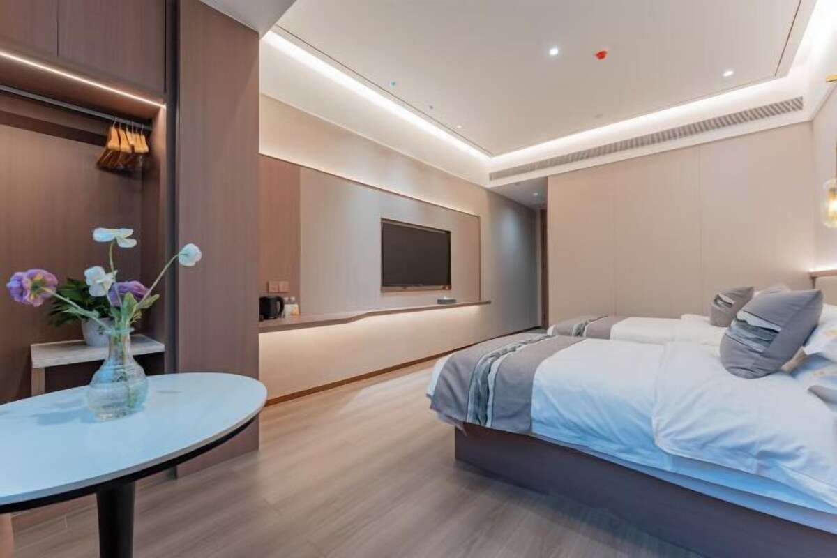 Ein modernes Hotelzimmer mit Bett, Fernseher, kleinem Tisch mit Blumenvase und Holzboden.