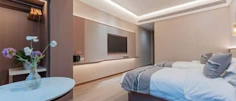 Habitación de hotel moderna con cama, televisor, una pequeña mesa con un jarrón de flores y piso de madera.