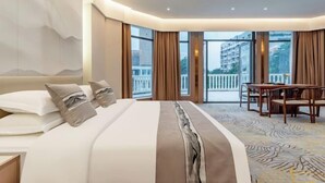 Ein modernes Hotelzimmer mit einem großen Bett, einem Essbereich und einem Balkon mit Blick auf die Stadt.