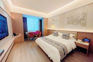 Ein Hotelzimmer mit einem großen Bett, einem Schreibtisch mit Stuhl, einem Fernseher und einem Wandbild.
