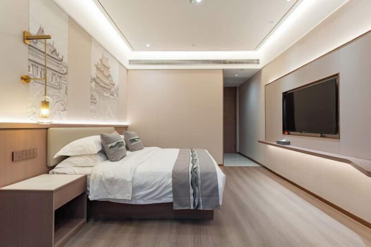A modern bedroom with a large bed, bedside tables, a TV mounted on the wall, and a ceiling light fixture.