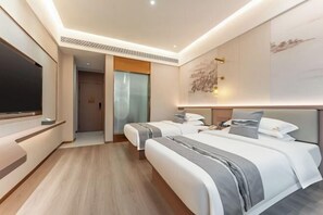Two single beds with grey and white bedding, a flat-screen TV, and a large artwork adorn this stylish room.