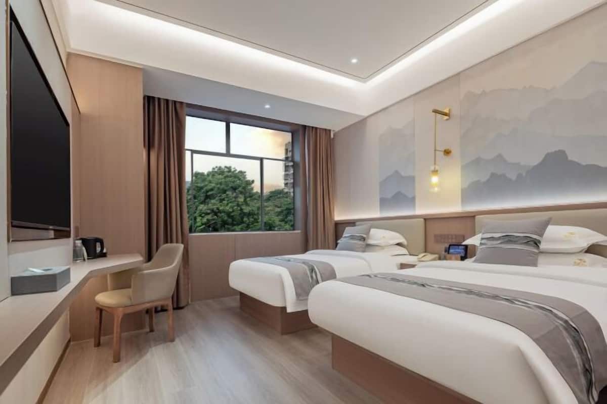 A hotel room with two beds, a desk, a chair, a TV, and a mountain view.