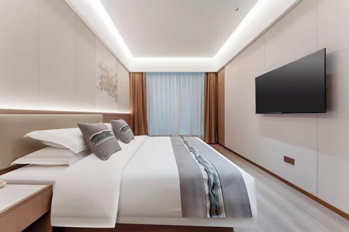 A modern hotel room with a large bed, a flat-screen TV, and a bedside table.