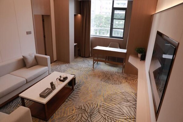 Ein modernes Hotelzimmer mit Sofa, Esstisch, Couchtisch und Fernseher.