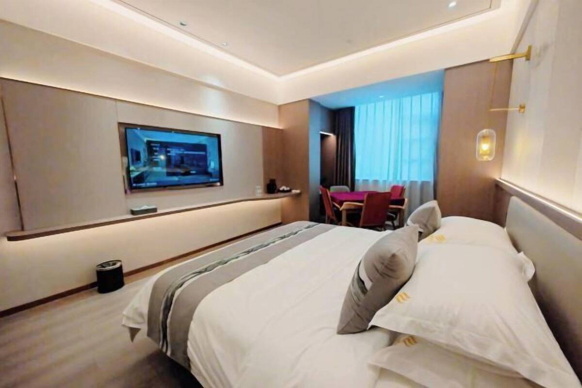 A hotel room with a bed, a TV mounted on the wall, a desk, and a chair.
