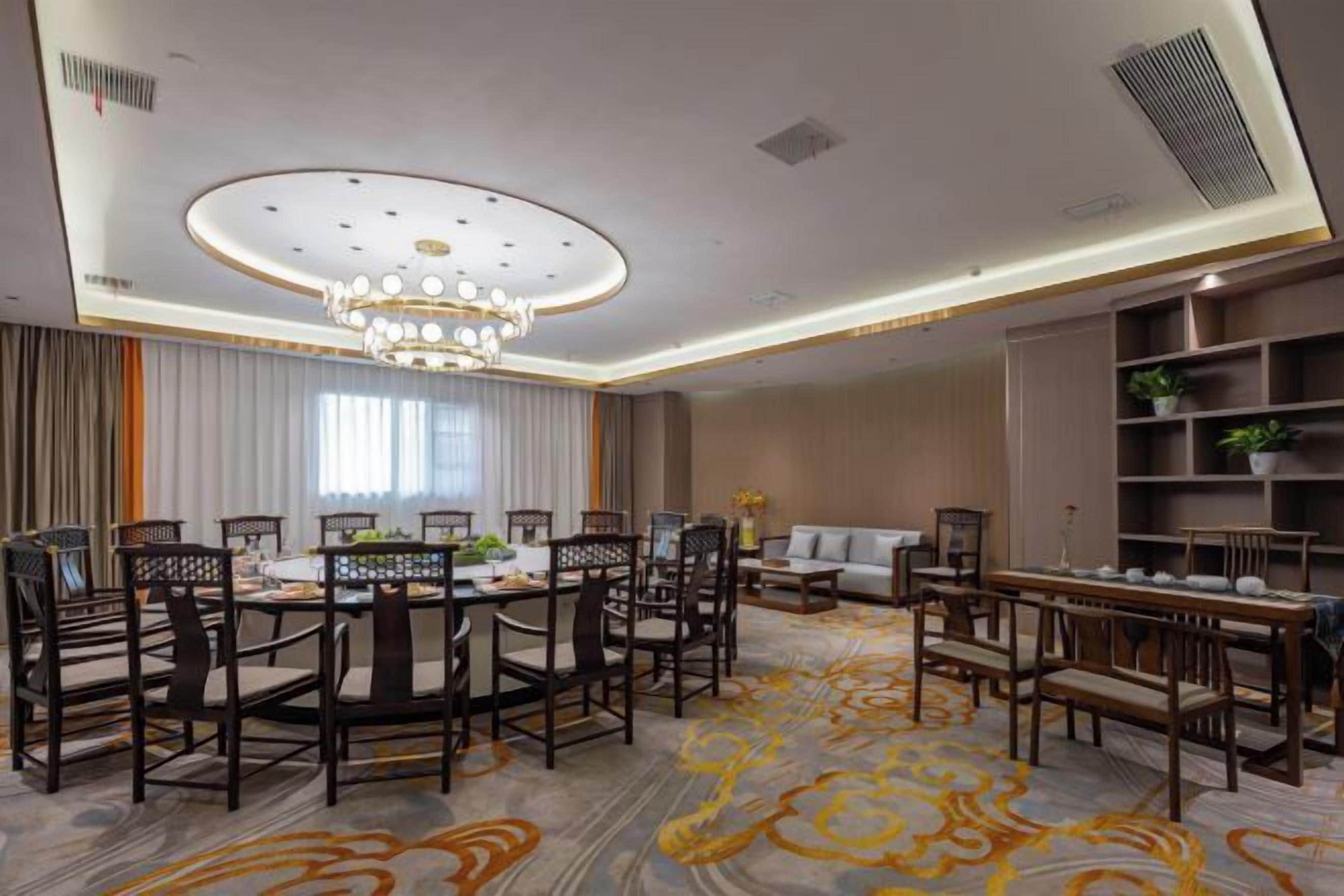 Une chambre d’hôtel avec une table de salle à manger ronde, des chaises, un canapé, une bibliothèque et un tapis à motifs.