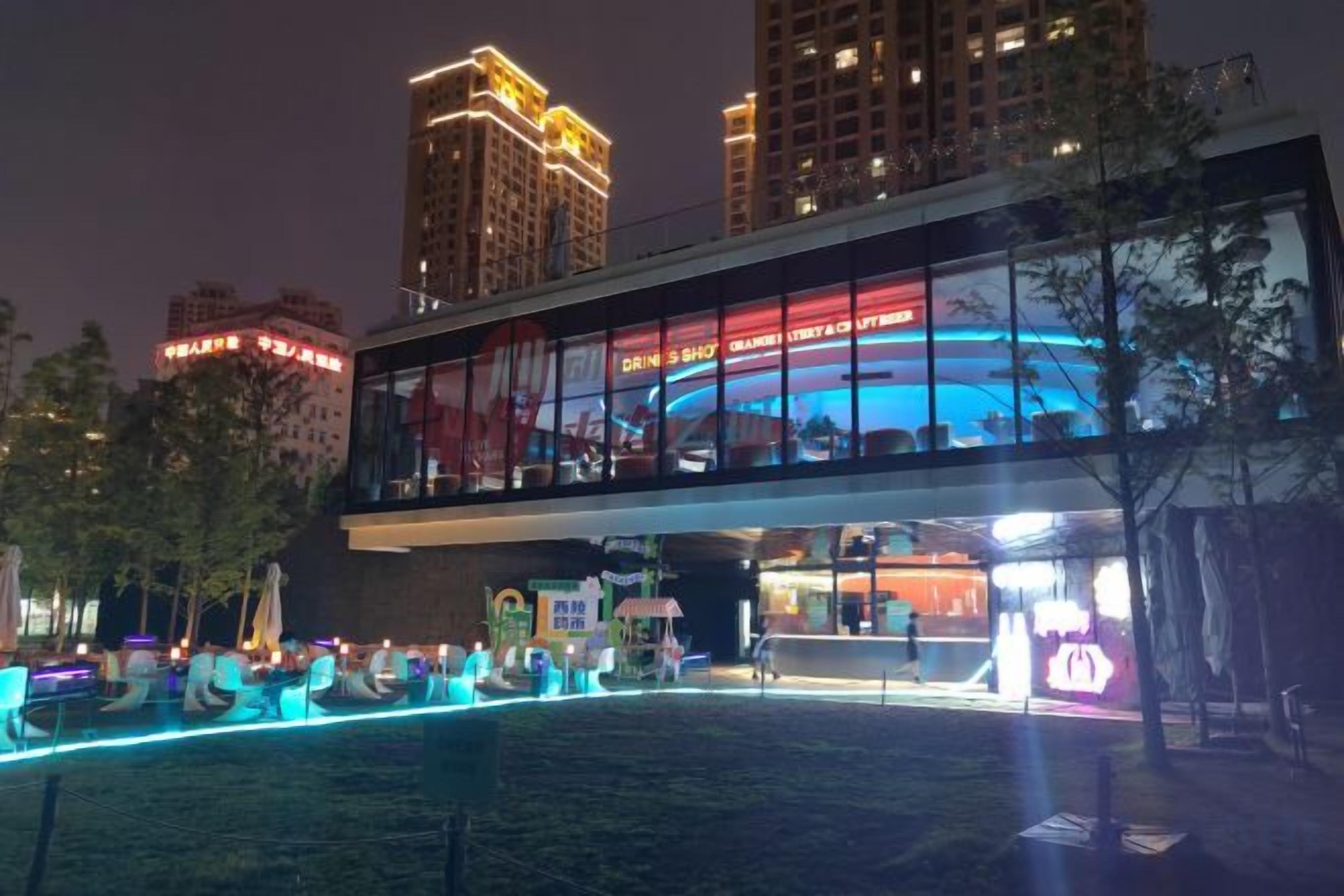 A modern building with a glass facade, a rooftop bar, and a neon-lit entrance.