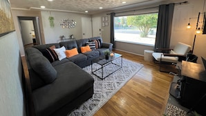 Un salon moderne avec un canapé d’angle, une table basse et une vue sur l’extérieur grâce à de grandes fenêtres.