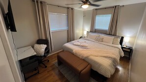 Une chambre à coucher comprenant un lit, un bureau, une chaise, un ventilateur de plafond et une fenêtre avec des stores.