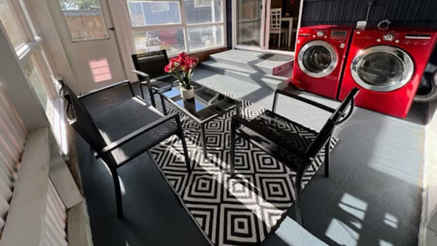 Une pièce baignée de lumière, avec un tapis à motifs noir et blanc, une table entourée de chaises et un lave-linge rouge.