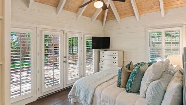 Une chambre à coucher avec un lit, un ventilateur de plafond, une télévision et une commode.