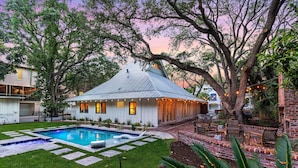 Une maison avec une piscine, entourée d’une terrasse en briques et de grands arbres.